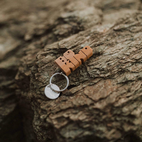 Trek Light BE KIND wood keychain on rustic rock background, featuring nickel split-ring. Unique hand-cut gift idea.