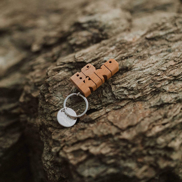 Trek Light BE KIND wood keychain on rustic rock background, featuring nickel split-ring. Unique hand-cut gift idea.