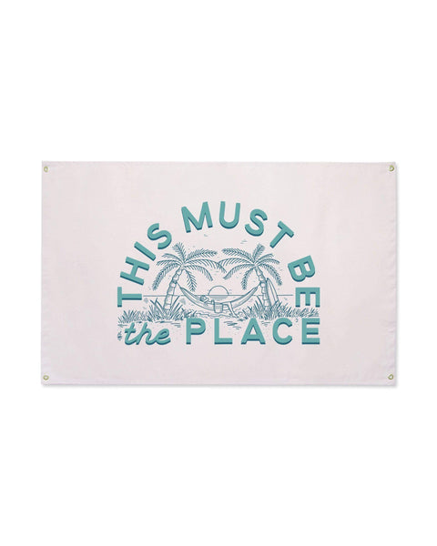 This Must Be The Place Canvas Flag in pale pink with teal palm tree and hammock print and grommets, on white.