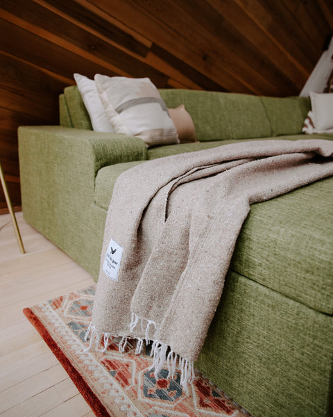 Trek Light Huntington Blanket draped over a cozy green couch, embodying beach vibes and comfort at home.
