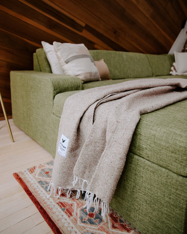 Trek Light Huntington Blanket draped over a cozy green couch, embodying beach vibes and comfort at home.