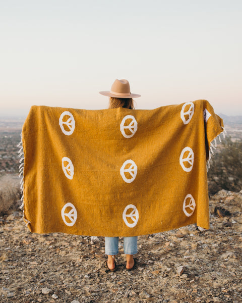 Person holding a beautiful handwoven Peace Blanket by Trek Light. made from recycled clothing materials, featuring peace symbols and vibrant yellow hue.