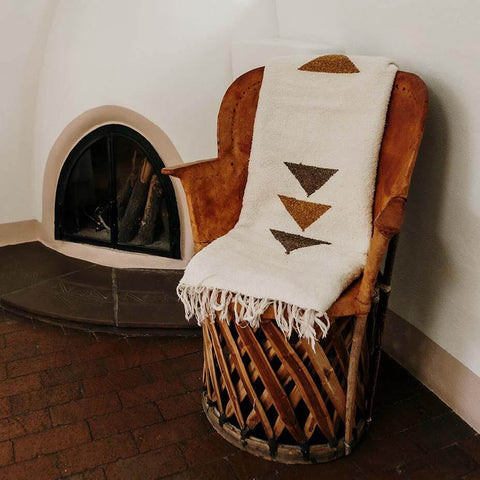 Cozy Summit Blanket, handwoven from recycled materials, draped over a chair by the fireplace, showcasing its beautiful design. By Trek Light.