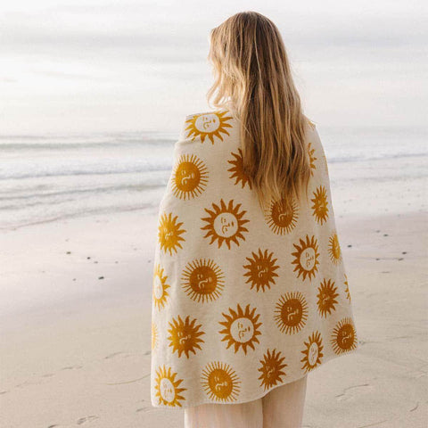 Person wrapped in sunny patterned blanket by the beach, enjoying warm comfort and tranquility.