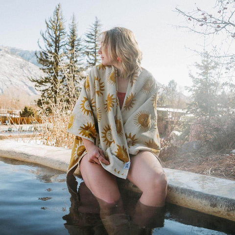 Woman wearing a comfy sun-patterned robe from Trek Light, relaxing in a scenic outdoor hot spring.