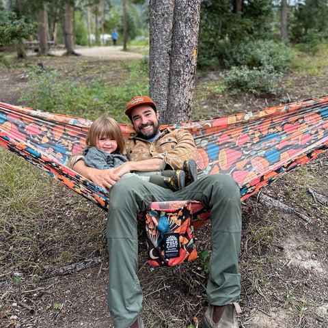 A parent and child lounging together in a Trek Light hammock in the forest