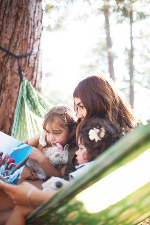 A woman and two children reading together in a Trek Light trout print hammock