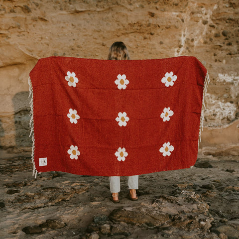 Woman holding a red Lazy Daisy handwoven blanket with white flower pattern