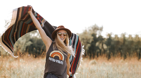 Woman in a sunny field waving a colorful Trek Light handwoven blanket