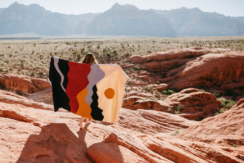 Person holding a colorful handwoven Trek Light blanket outdoors with mountains behind