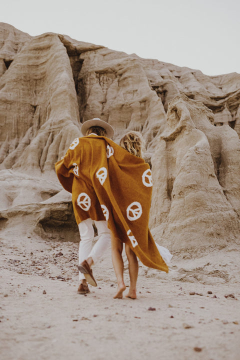 Two people wrapped in a handwoven Trek Light Peace Blanket in front of desert rock formations