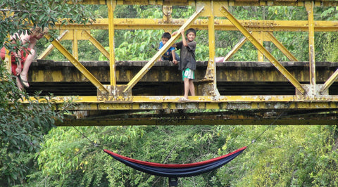 Red and navy Trek Light hammock hung beneath the yellow bridge over the Cahabon River at Semuc Champey, Guatemala, as kids watch from above