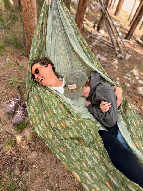 Two people relaxing in a Trek Light River Trout Print double hammock in a forest
