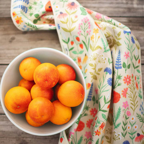 Wildflower Wonder kitchen towel with vibrant floral pattern beside a bowl of fresh oranges
