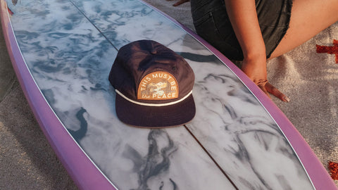 Stylish "This Must Be the Place" hat on a surfboard, perfect for Trek Light adventures.