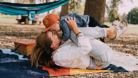 Mother and child enjoy outdoor playtime on a Trek Light picnic blanket, with a hammock in the background, perfect for family fun.