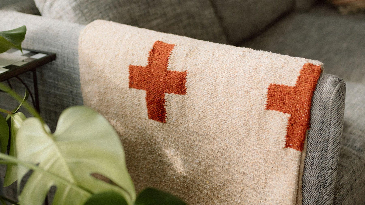 Cozy Trek Light pattern blanket with orange crosses draped over a sofa armrest, adding warmth and style to your living room.