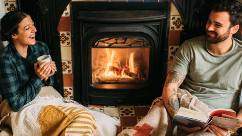 Cozy couple by the fireplace, wrapped in Trek Light gear, sharing laughter and warmth. Perfect holiday gift idea for comfort lovers.