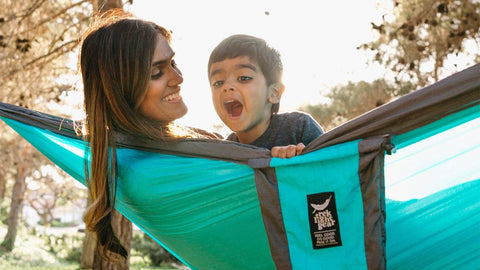 Relaxing in a Trek Light hammock, a delighted family enjoys sunshine and nature together.