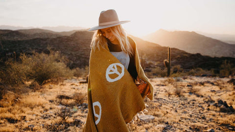 Woman wrapped in a Trek Light blanket with peace symbols at sunset in a desert landscape