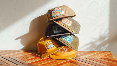 Colorful Trek Light caps stacked on a wooden table, featuring unique embroidered designs perfect for outdoor adventures.