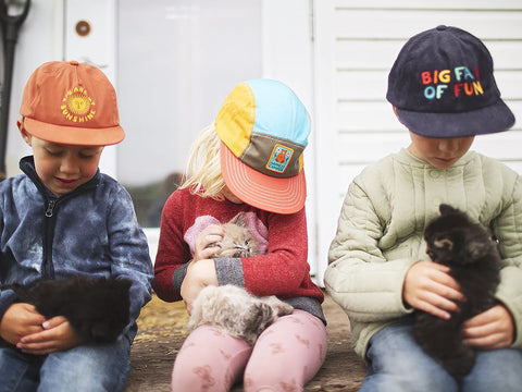 Smiling kids wearing Trek Light hats sitting with kittens