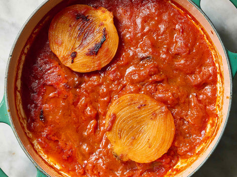 Hearty tomato sauce in a green pot with two whole onions on top, showcasing a rich red color and thick texture, ideal for pasta dishes.