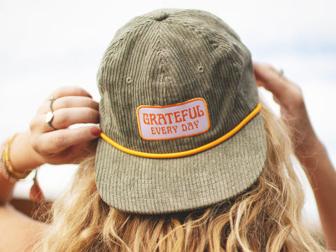 Woman wearing green hat with 'Grateful Every Day' embroidered on it, showcasing positive attitude and fashion.