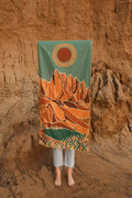 Trek Light towel with mountain and sun design held in front of rocky backdrop, blending nature and art for outdoor adventures.