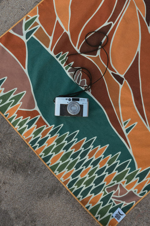 Vintage camera resting on a colorful Trek Light blanket with geometric patterns, capturing the essence of creative outdoor photography.