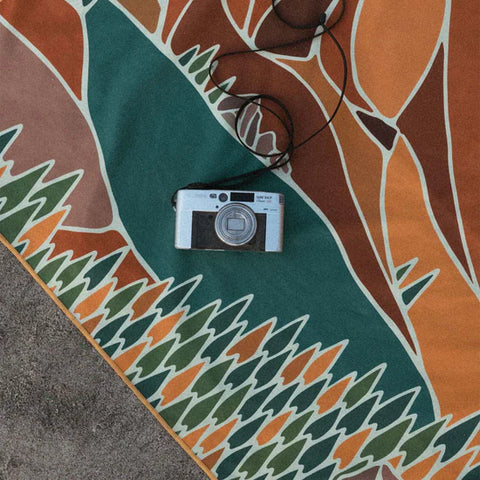 Retro camera resting on a vibrant Trek Light picnic blanket with abstract nature design, perfect for outdoor adventures.