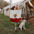 Person holding Trek Light Arizona Blankestry with desert cactus design near a tent, accompanied by a white dog.