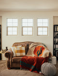 Cozy Trek Light Arizona Blanket on a couch, handwoven from recycled materials, featuring a desert sunset and cactus design. Beautiful and versatile.