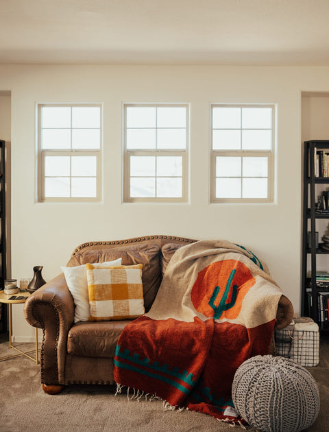 Cozy Trek Light Arizona Blanket on a couch, handwoven from recycled materials, featuring a desert sunset and cactus design. Beautiful and versatile.