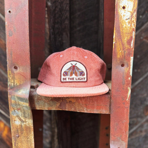 Be The Light Hat displayed on a rustic rack, showcasing its unique design and message.