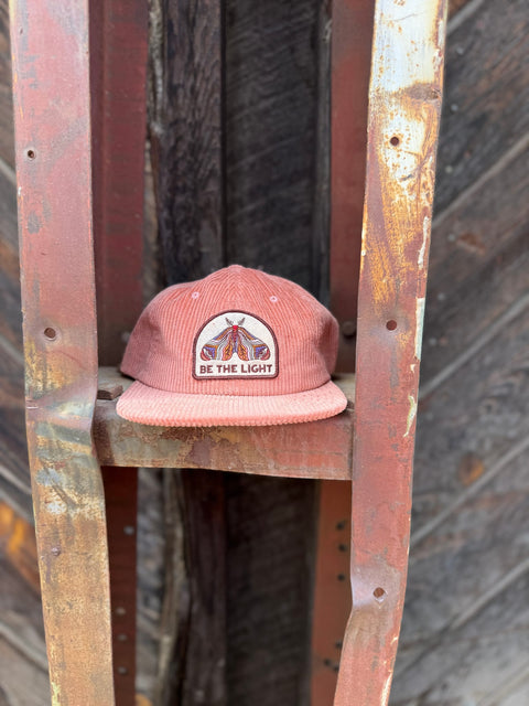 Be The Light Hat displayed on a rustic rack, showcasing its unique design and message.