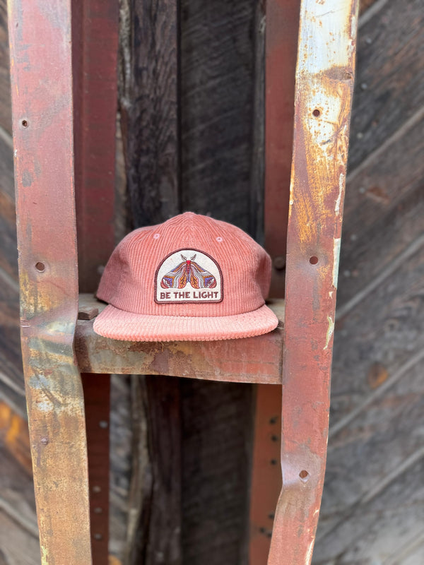 Be The Light Hat displayed on a rustic rack, showcasing its unique design and message.
