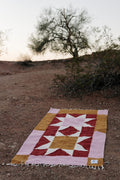 Beautiful handwoven Bernie Blanket made from recycled clothing, lying on desert ground, versatile and cozy. By Trek Light.