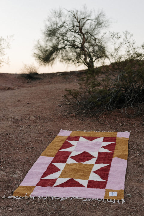 Beautiful handwoven Bernie Blanket made from recycled clothing, lying on desert ground, versatile and cozy. By Trek Light.