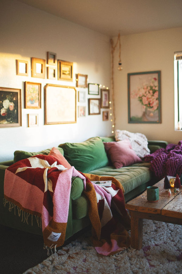 Cozy living room with the beautiful Bernie Blanket, handwoven using recycled clothing materials draped over a green sofa. By Trek Light.