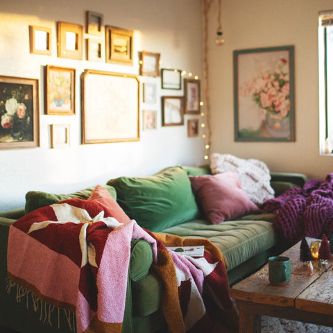 Cozy living room with the beautiful Bernie Blanket, handwoven using recycled clothing materials draped over a green sofa. By Trek Light.