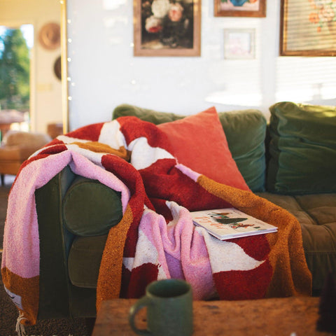 Cozy Bernie Blanket made from recycled clothing materials, handwoven and versatile, draped over a couch for a warm, inviting look. By Trek Light.