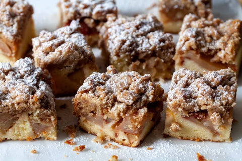 Close-up of freshly baked apple crumble cake squares dusted with powdered sugar on a white surface.