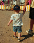 Toddler walking in the park wearing a Big Fan Of Fun Kids Hat, holding an adult's hand, enjoying a day out.