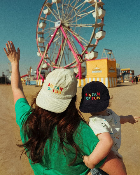 Two people wearing Big Fan Of Fun Hat - Twinsie Set enjoying a carnival scene with a ferris wheel.