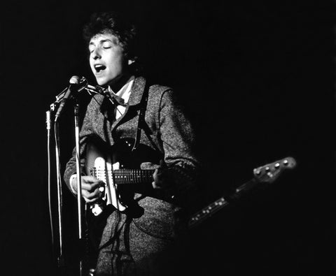 Musician performing live on stage, playing an electric guitar and singing into a microphone, black and white photo, moody lighting.