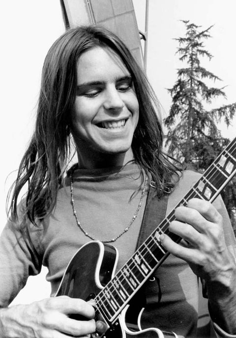 Person playing electric guitar outdoors with long hair and a joyful expression.