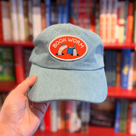 Handheld Book Worm Hat displayed in front of a colorful bookshelf; adjustable fit and designed for comfort.