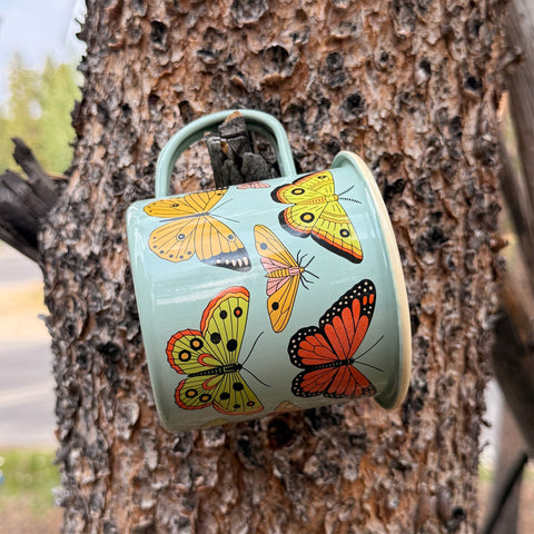 Butterfly Beauty Mug - Enamel 16oz Mug hanging on a tree, featuring beautiful butterfly designs.