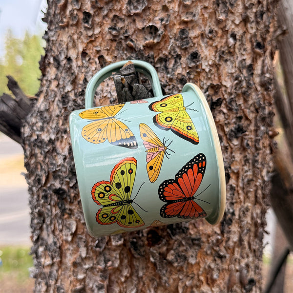 Butterfly Beauty Mug - Enamel 16oz Mug hanging on a tree, featuring beautiful butterfly designs.